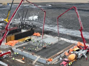 Cranes pouring concrete and workers leveling out concrete.